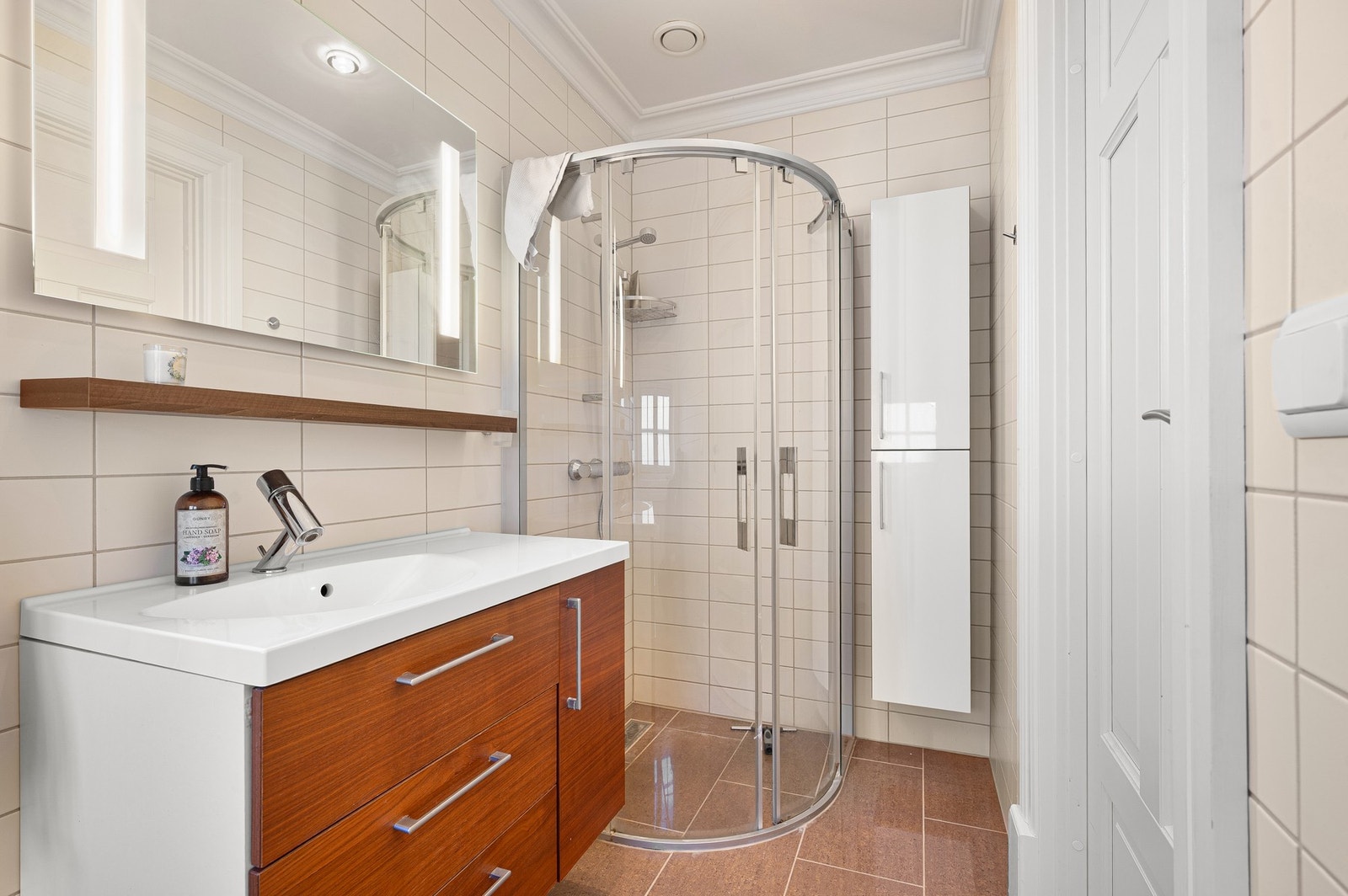 Pent flislagt bad med dusjhjørne, moderne innredning og praktisk oppbevaringsplass. Galleribilde