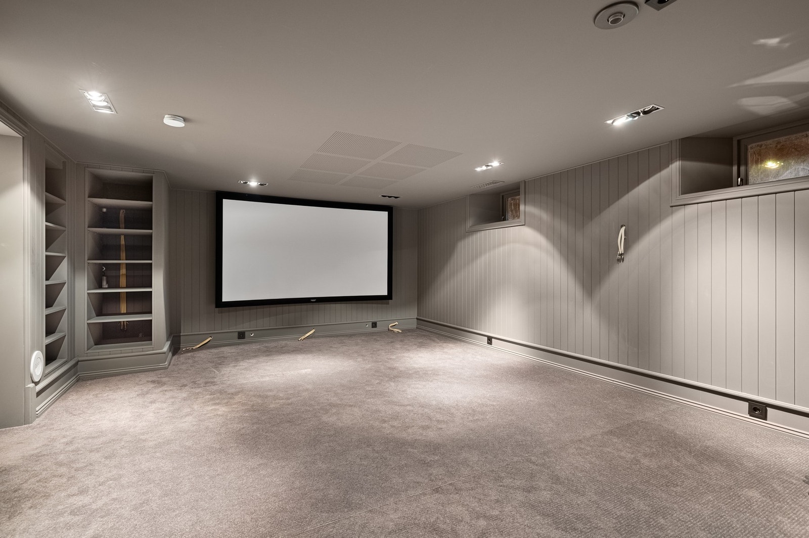 Stor og lun underetasjestue med prosjektoroppsett og god plass til sofa og loungemiljø. Galleribilde