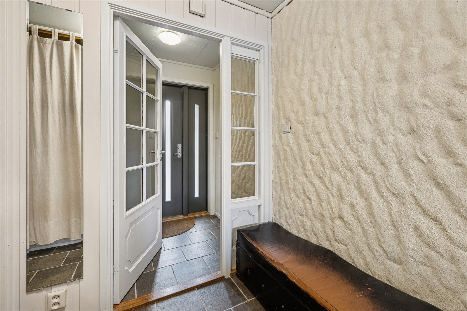 Via ytterdør, som var ny i 2017, er det inngang til romslig entré på halvplan med lyse, malte vegger og flislagt gulv. Galleribilde