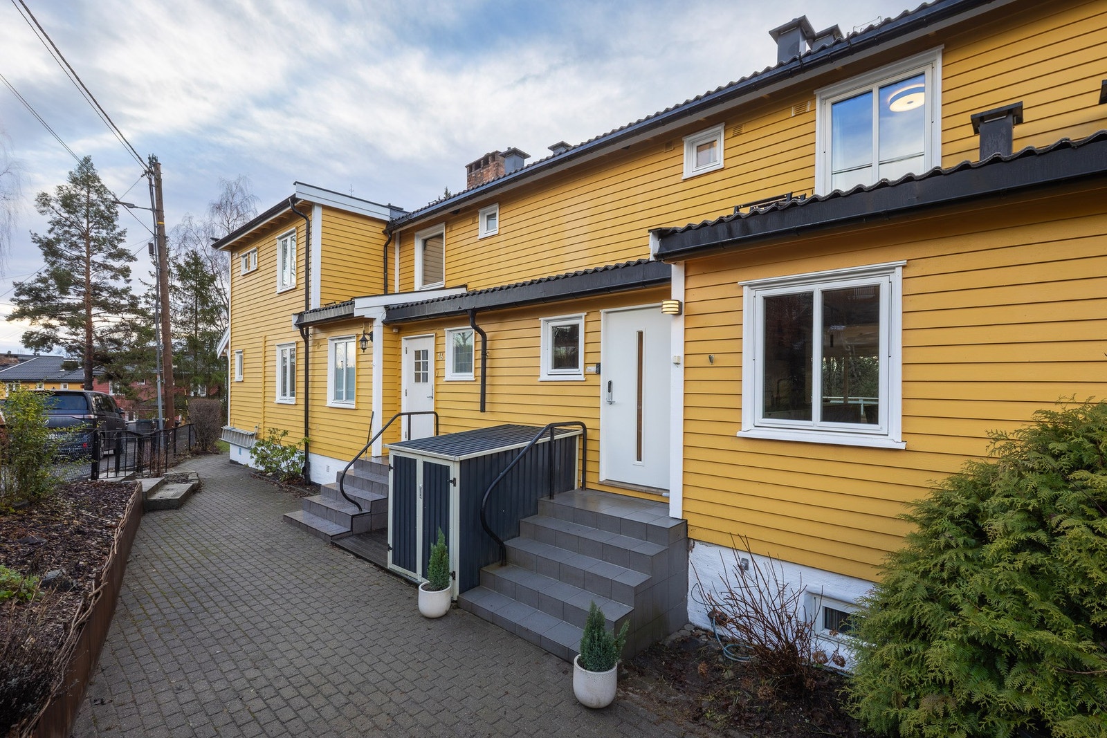 Utebod i tilknytning til inngangssiden. Pent opparbeidet blomsterbed med lettstelte stauder og delvis vintergrønn liguster hekk Galleribilde