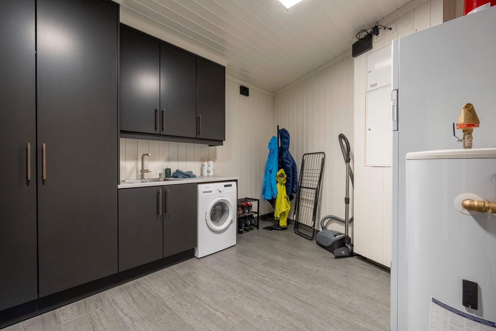 Vaskerommet har flislagt gulv med oppkant, malte panelvegger og paneltak. Vaskerommet har også rikelig med oppbevaringsplass i plassbygd innredning fra Brusveen Snekkerverksted AS. Galleribilde