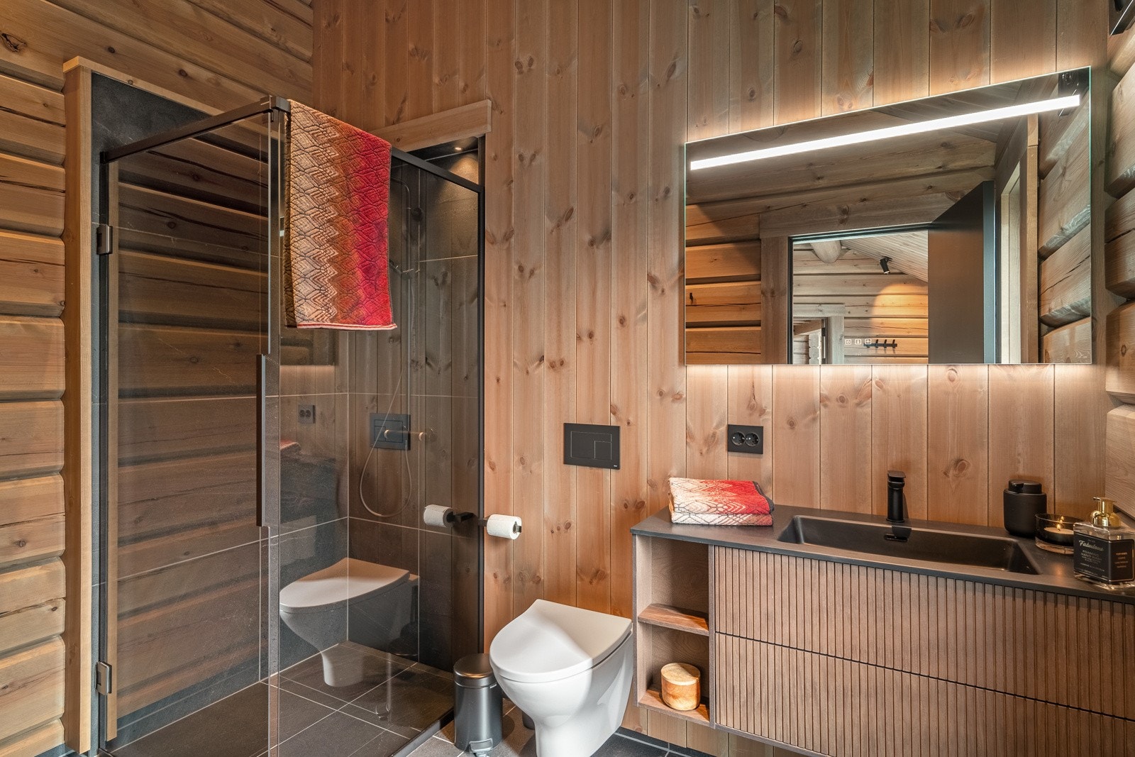 Badet tilknyttet hovedsoverommet er stilfullt utført med delikate fliser på gulvet og veggene i dusjsonen, kombinert med tømmervegger og en vegg kledd med stående panel fra Vyrk. Ifølge selger blir servanten byttet med en benkeplate og bollevask. Galleribilde