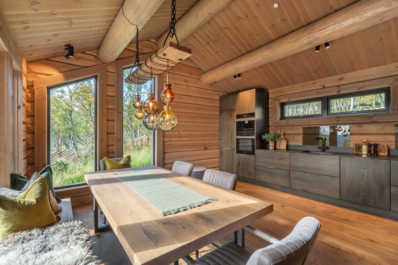 Kjøkkenet og spisestuen har de samme overflatene som stuen, herunder lekker eikeparkett på gulv, flotte tømmervegger og paneltak, samt gjennomført belysning i himling og vannbåren gulvvarme. Galleribilde