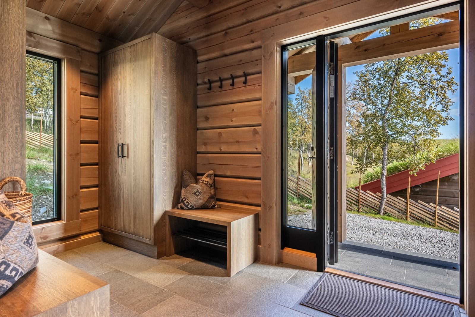 Vel inne blir du møtt av en innbydende entré med vakker Offerdal skifer på gulvet, lune tømmervegger og god takhøyde. Yttertøy kan oppbevares i to plassbygde garderobeskap fra Brusveen Snekkerverksted AS, med beisede trefronter og stilrene håndtak. Galleribilde