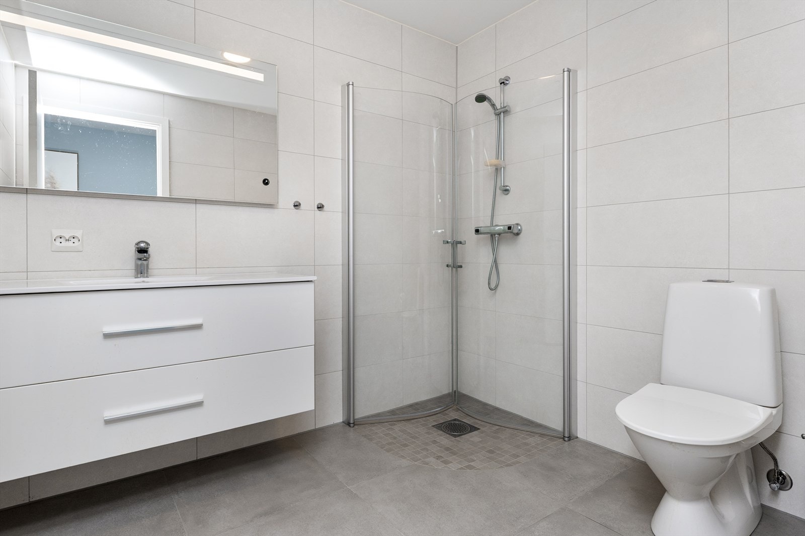 Flislagt bad med elektriske varmekabler på gulv. Klassisk lys innredning med servant, dusjhjørne og toalett. Galleribilde