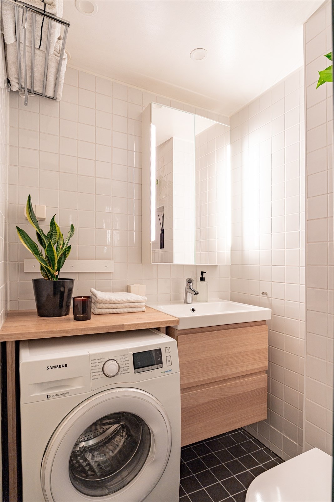 Baderomsinnredningen består av et vegghengt toalett, nedsenket dusjsone med glassvegg i tillegg til vegghengte baderomsskuffer med servant og overhengt speilskap. Galleribilde