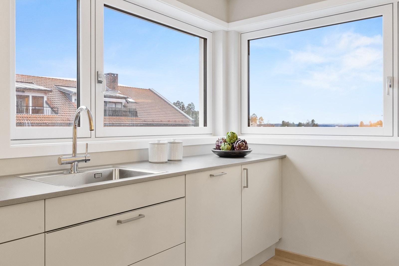 Kjøkkenets store hjørnevindu åpner opp mot nærområdet og slipper inn rikelig med dagslys. En nydelig plass å stå og forberede måltider og se på været. Galleribilde