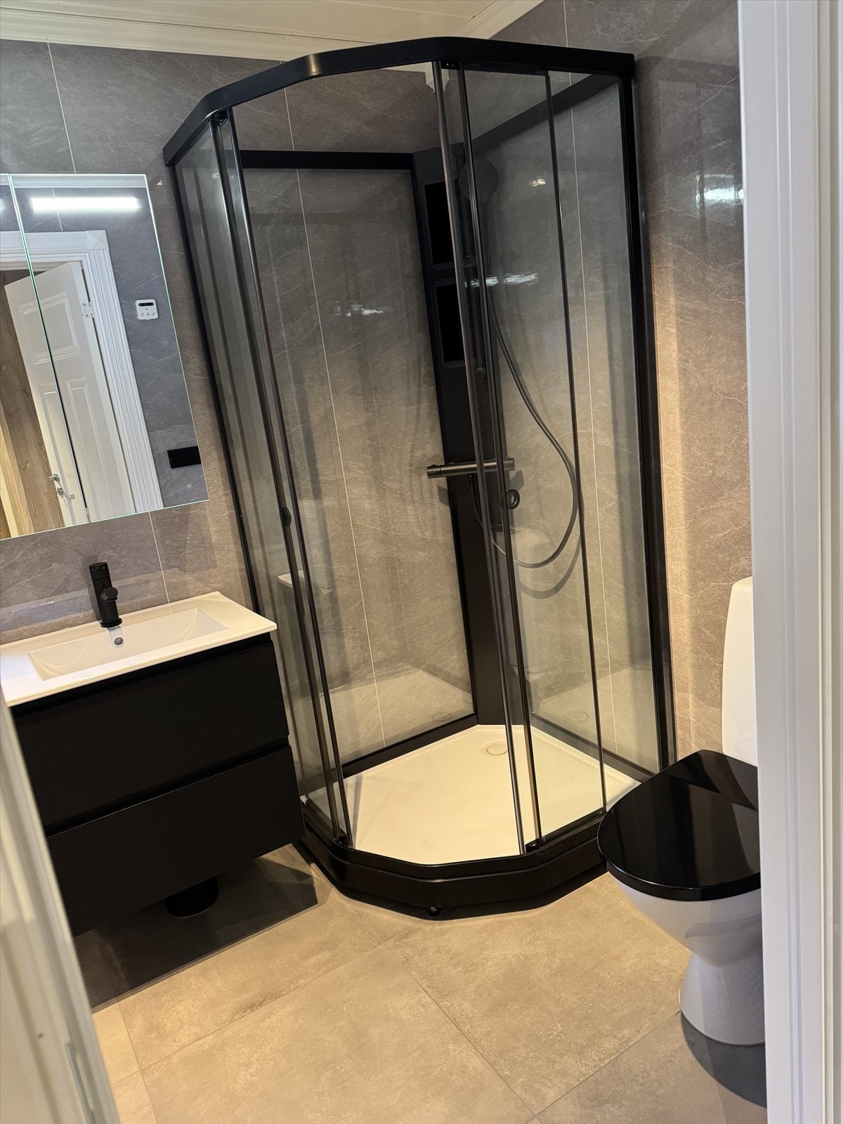 Bad med fliser på gulv, våtromsplater, dusjkabinnet, toalett og servant med speilskap. Galleribilde