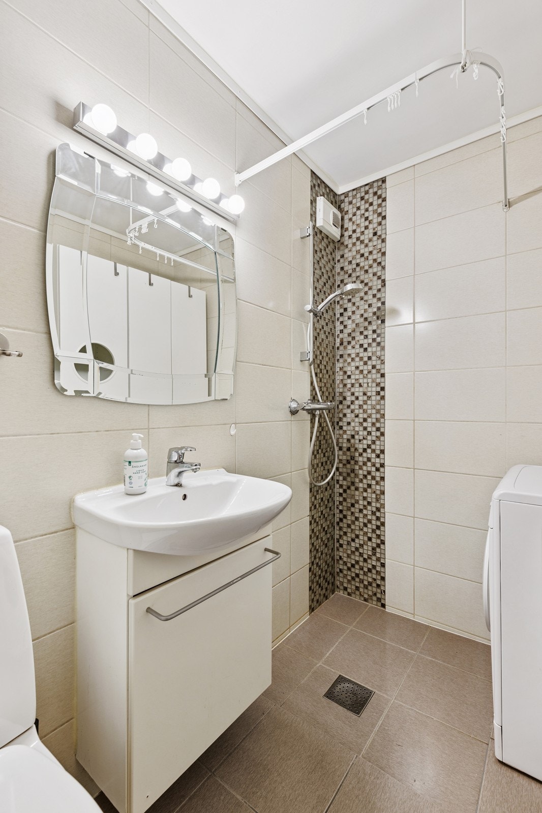 Pent flislagt bad med oppbevaring underservant i tillegg til skap rundt vaskemaskinen. Galleribilde