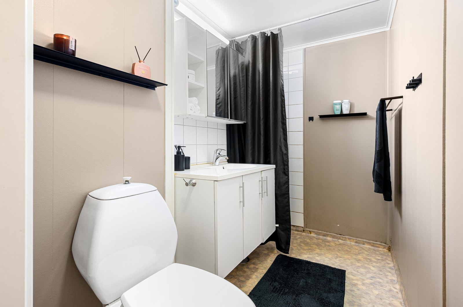 Badet er utstyrt med åpen dusjløsning med forheng m/termostatstyrt blandebatteri og gulvmontert toalett. Galleribilde