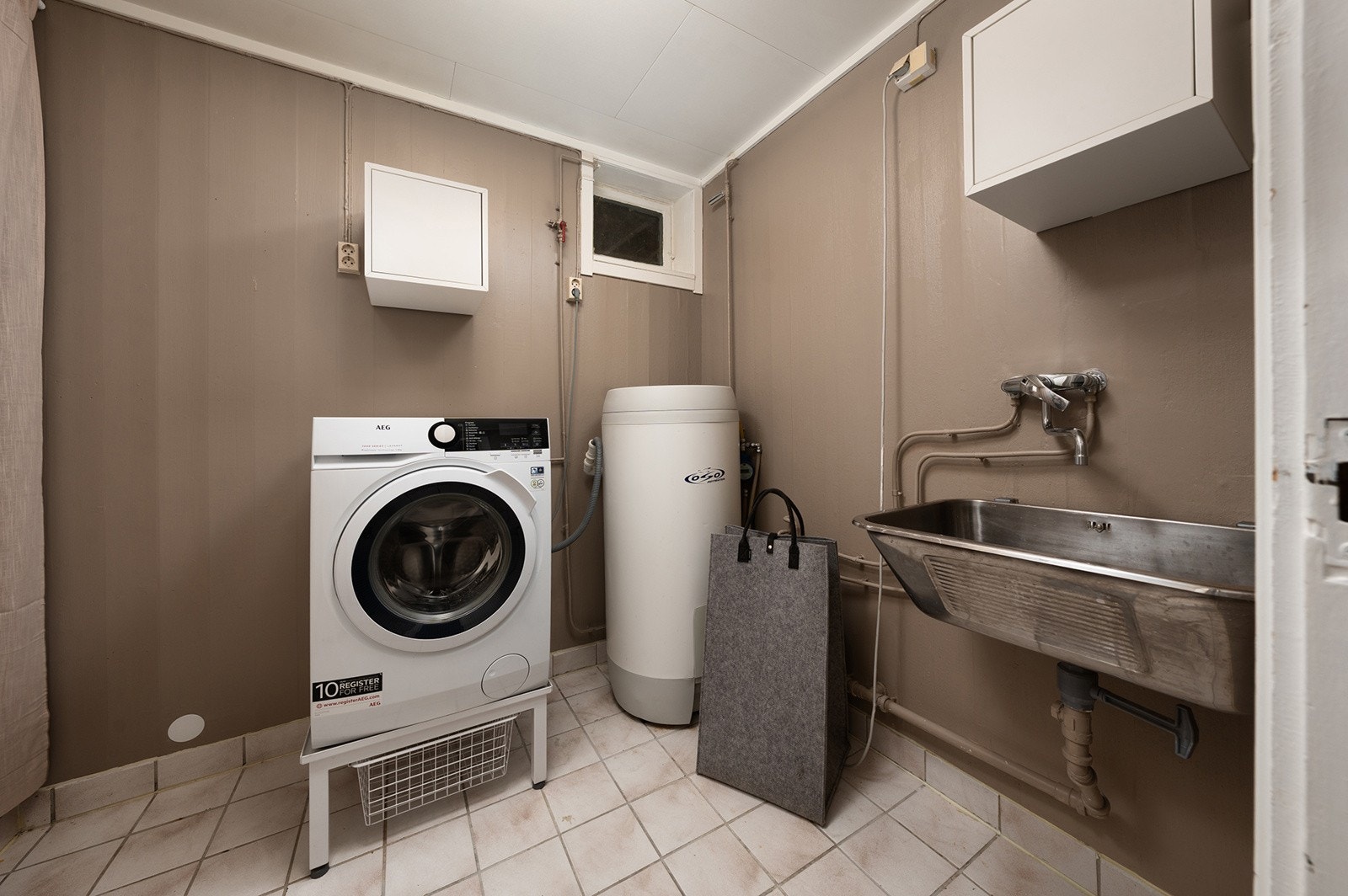 Romslig og praktisk vaskerom/bod med flislagt gulv og malte vegger. Galleribilde