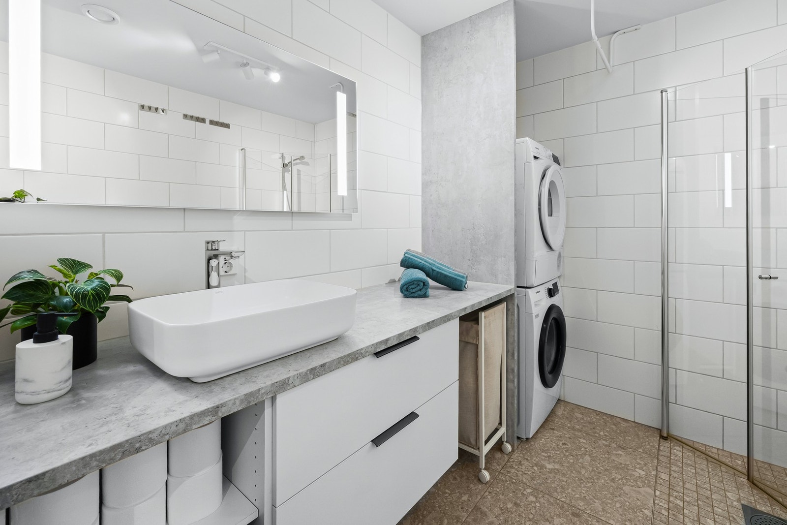 Delikat bad med flislagte overflater og varmekabler i gulv. Innredningen består av moderne servantmøblement med 2 skuffer samt hyller, forlenget benkeplate med servant og speil med integrert belysning. Galleribilde