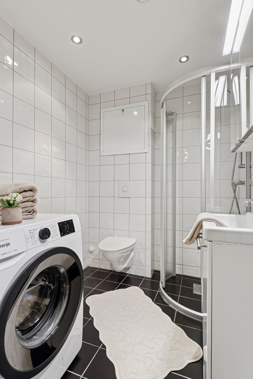 Badet er tidløst innredet med en kombinasjon av sorte og hvite fliser på vegger og gulv. I gulvet har man også varmekabler for ekstra komfort. Galleribilde