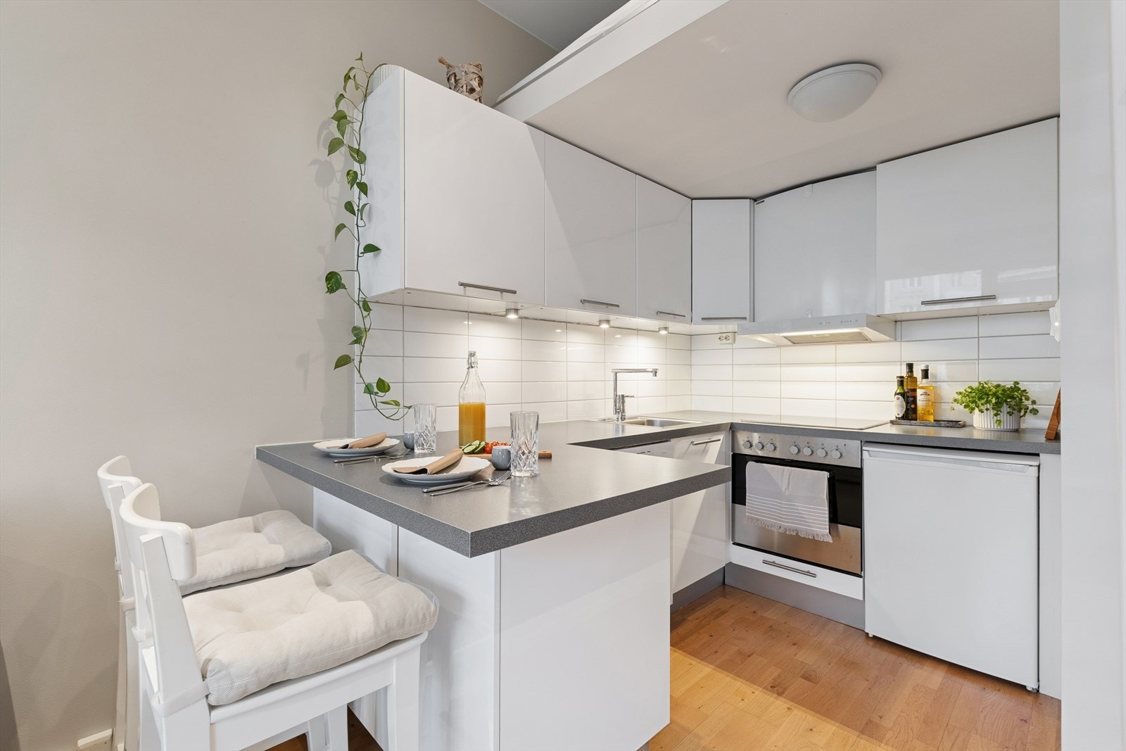 Kjøkkenet er innredet med hvite, slette fronter og grå benkeplate i laminat. Her har man godt med skapplass og gode arbeidsflater på benk. Det er i tillegg laget til en barløsning for best mulig utnyttelse av arealet. Galleribilde