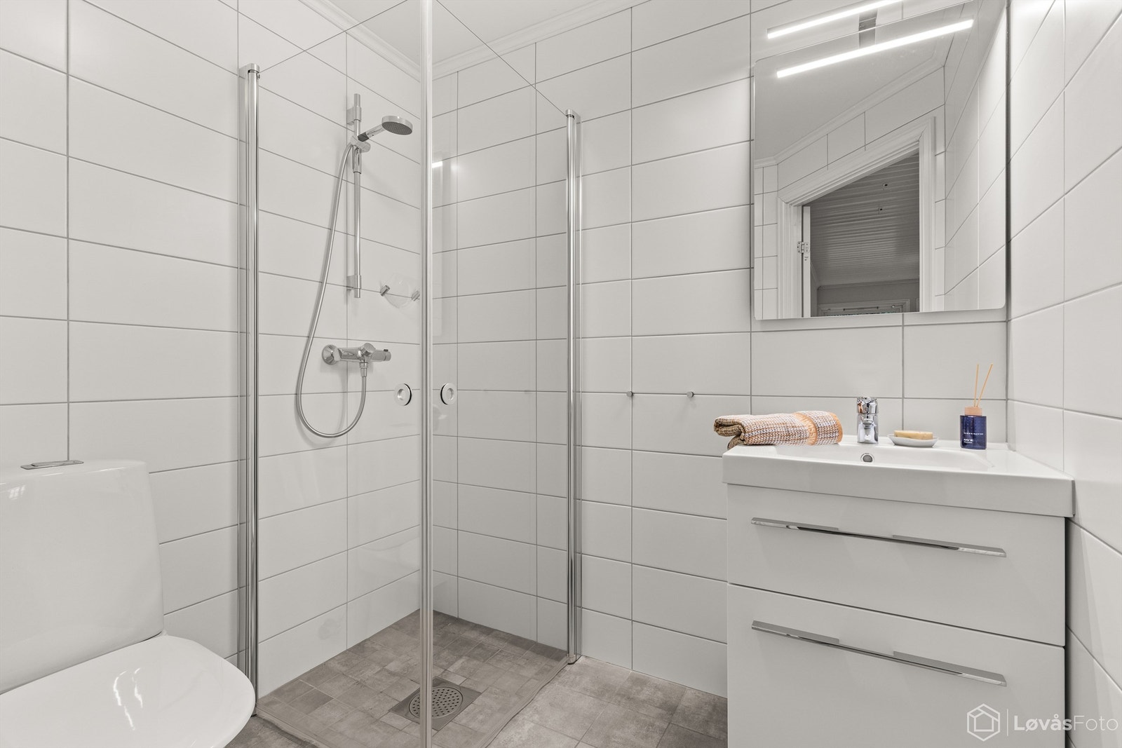 Baderommet i kjelleren ble renovert i 2016 og fremstår som moderne og funksjonelt. Det er helfliset med gulvvarme og har en vegghengt servantinnredning med skuffer, speil med overlys, og et dusjhjørne med glassdører, samt toalett. Galleribilde