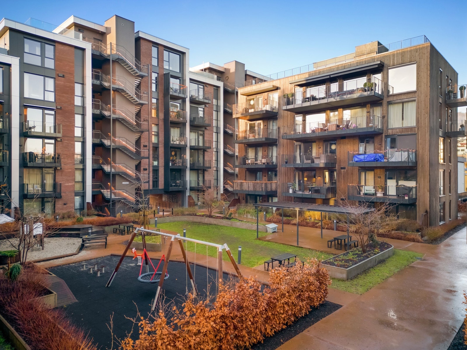 Felles atrium i midten av bygningene som er pent opparbeidet med grøntarealer, flere sittebenker og lekeplass Galleribilde