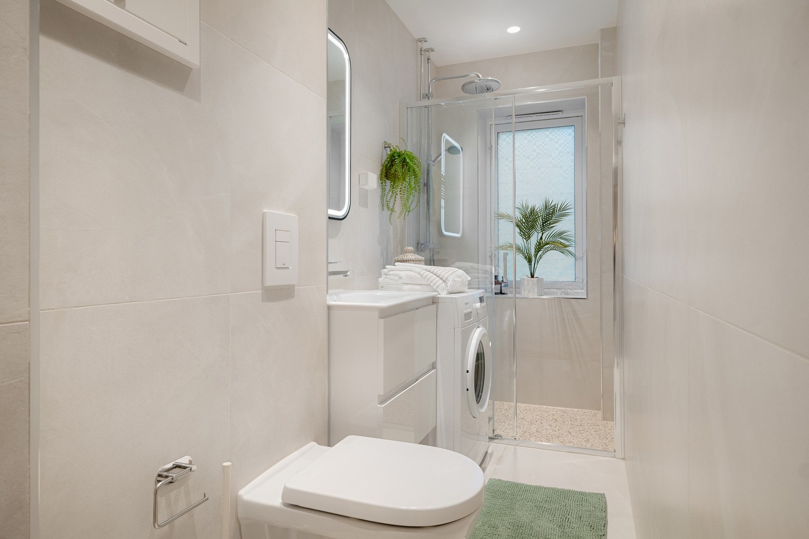 Rommet er innredet med servantskap med heldekkende servant, speil med integrert belysning, vegghengt toalett og dusjhjørne med glassvegger. Galleribilde