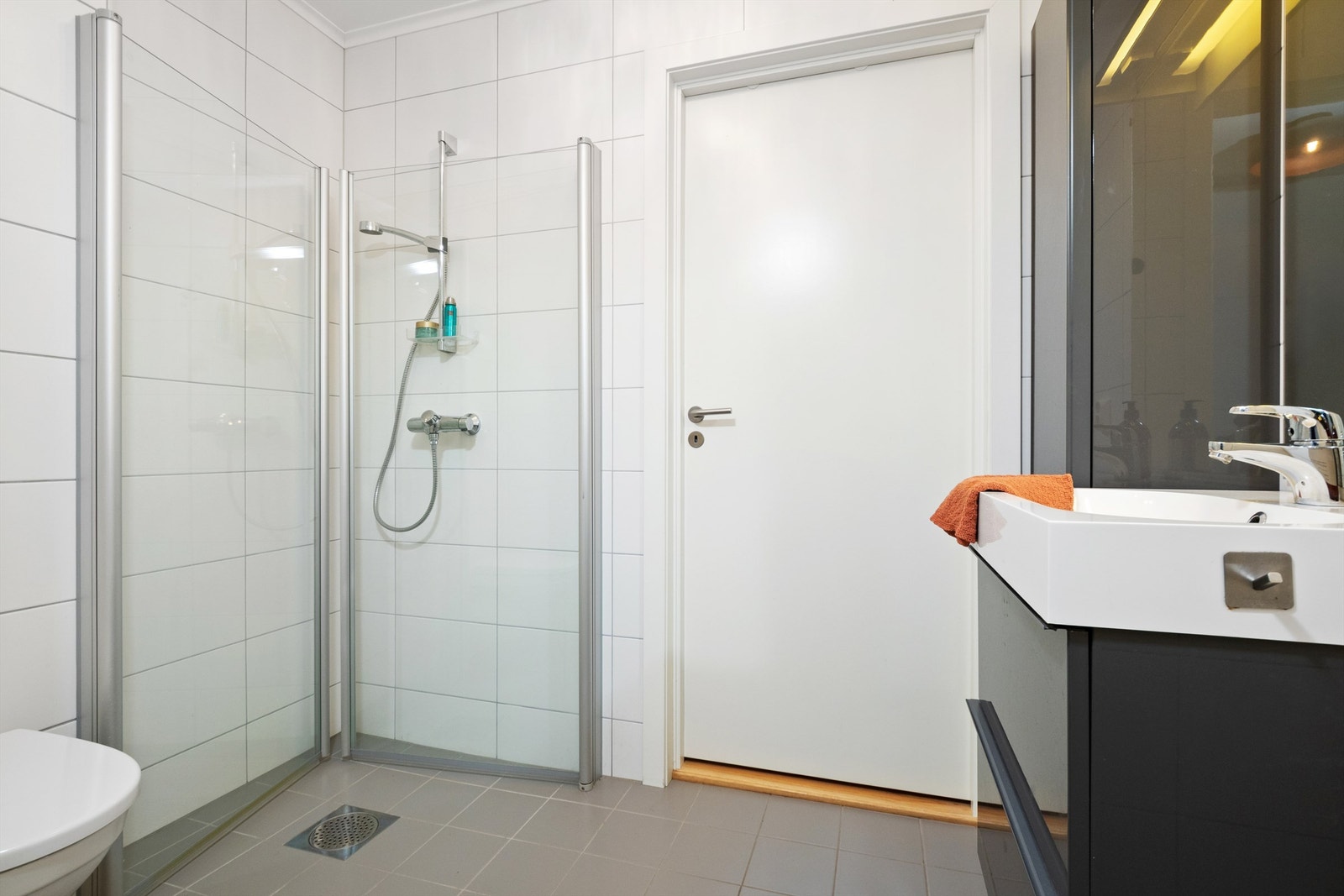 Flislagt baderom med innredning med servant, vegghengt toalett og dusjhjørne. Galleribilde