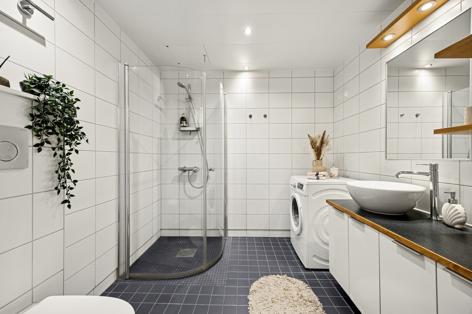 Flislagt bad med gulvvarme, downlights, praktisk innredning med servant på benkeplate, speil med belysning for komfort. Galleribilde