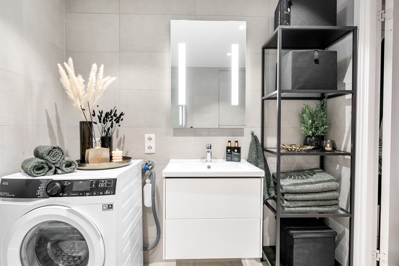 Badet er utstyrt med veggmonterte dusjdører, servant med underskap, speil med lys, veggmontert wc og opplegg for vaskemaskin. Galleribilde