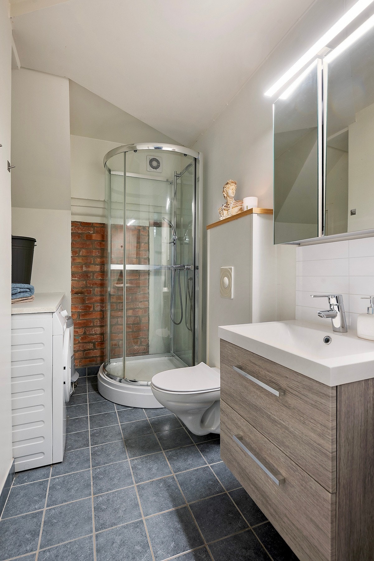 Badet har flislagt gulv med varmekabler, og god oppbevaringsplass i servantinnredning og speilskap Galleribilde