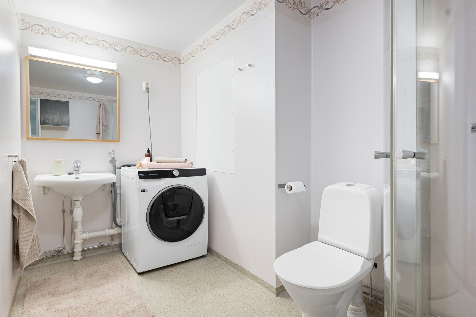 Rommet utstyrt med opplegg for vaskemaskin, veggmontert servantskål, toalett og dusjhjørne med innfellbare glassdører. Galleribilde