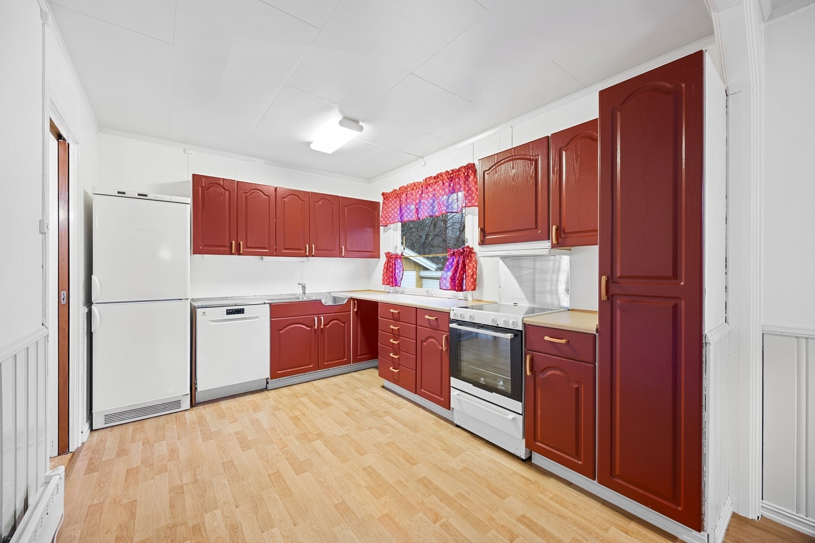 Innredningen er eldre med røde, profilerte fronter, laminat benkeplate og benk med stålbeslag. Galleribilde