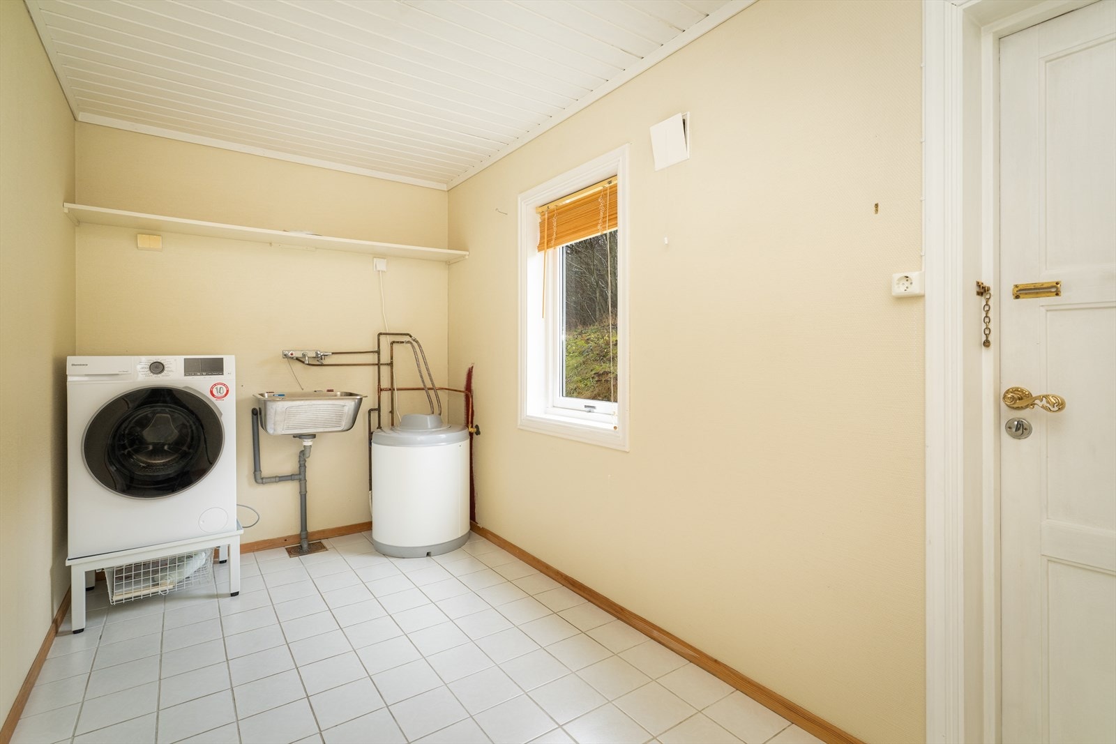 Boligen har eget praktisk vaskerom med egen utgangsdør. Her er det skyllekum og opplegg for vaskemaskin, og det er god plass til klestørken. Varmtvannstanken fra 2021 på 80 liter er også plassert her. Galleribilde