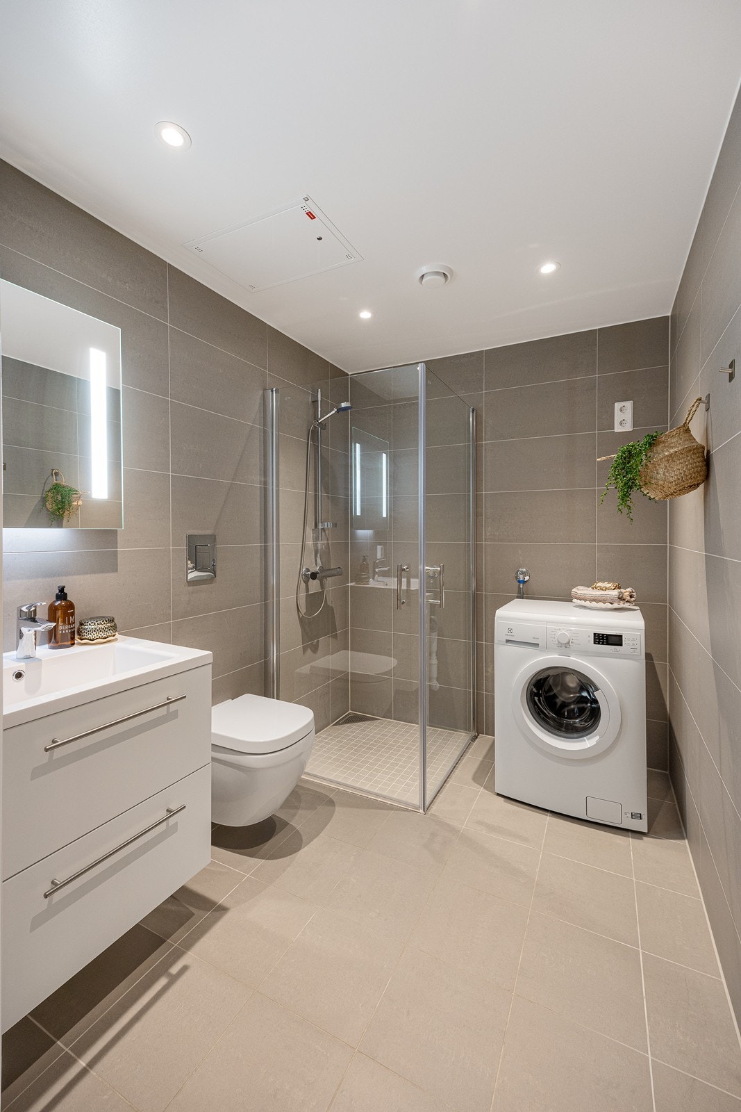 Badet er innredet med servant i baderomsinnredning, vegghengt toalett, dusjhjørne med innfellbare glassvegger og opplegg for vaskemaskin. Galleribilde