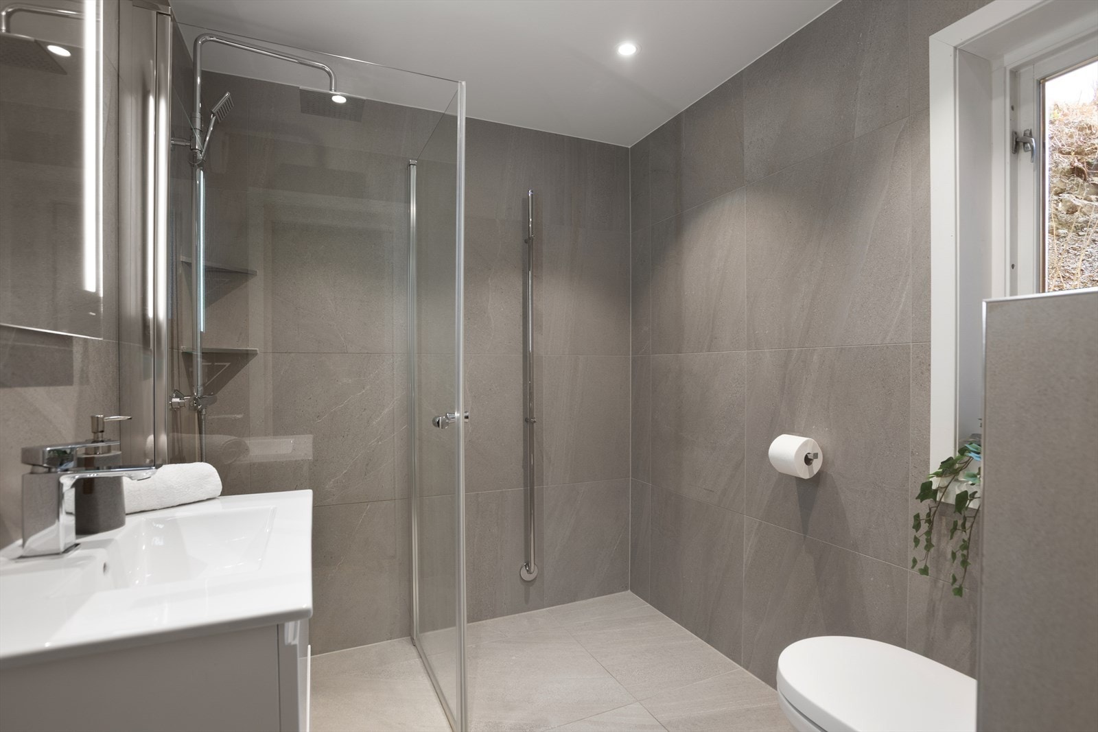 Hovedbadet ble totalrenovert i 2020 av fagfirma, og fremstår moderne og velholdt med flislagte overflater, gulvvarme, vegghengt toalett med innebygd sisterne, servantinnredning, speil med belysning og dusjsone med glassdører. Galleribilde