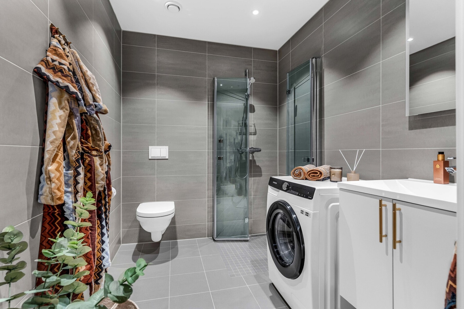 Delikat og moderne baderom fra byggeåret 2024 med behagelig gulvvarme, vegghengt toalett, dusjhjørne, servantskap, speil og opplegg for vaskemaskin. Galleribilde