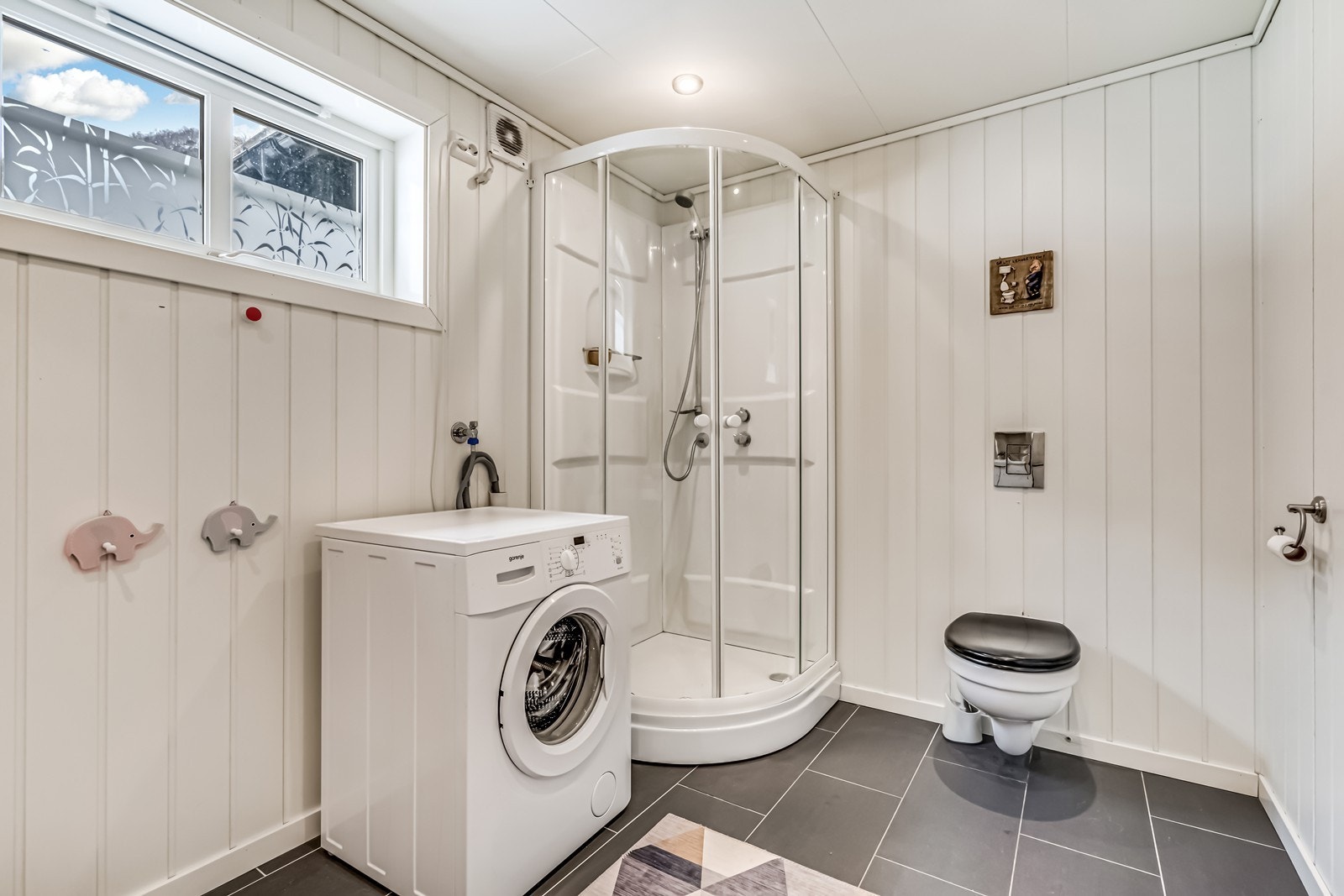 Rommelig bad med dusj, toalett, vask i seksjon og opplegg for vaskemaskin. Galleribilde