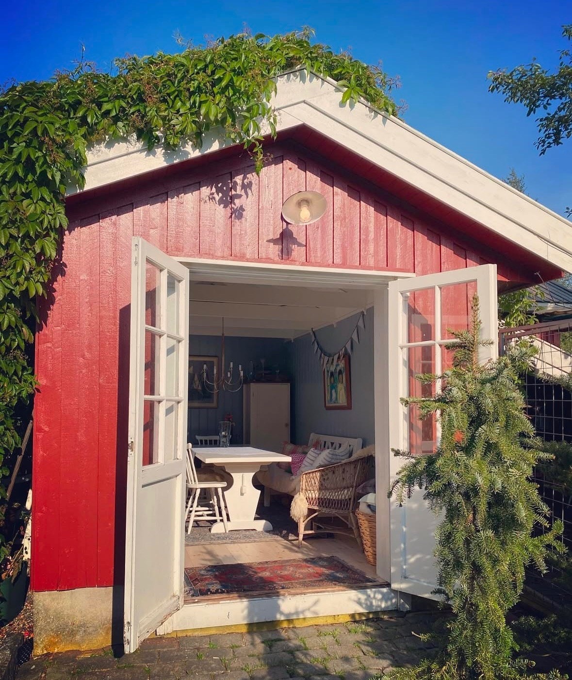 Tofløyede glassdører fører inn til hagestuen med tak dekket av en frodig rådhusvillvin som blir omtrent like rød som husveggen om høsten. Galleribilde