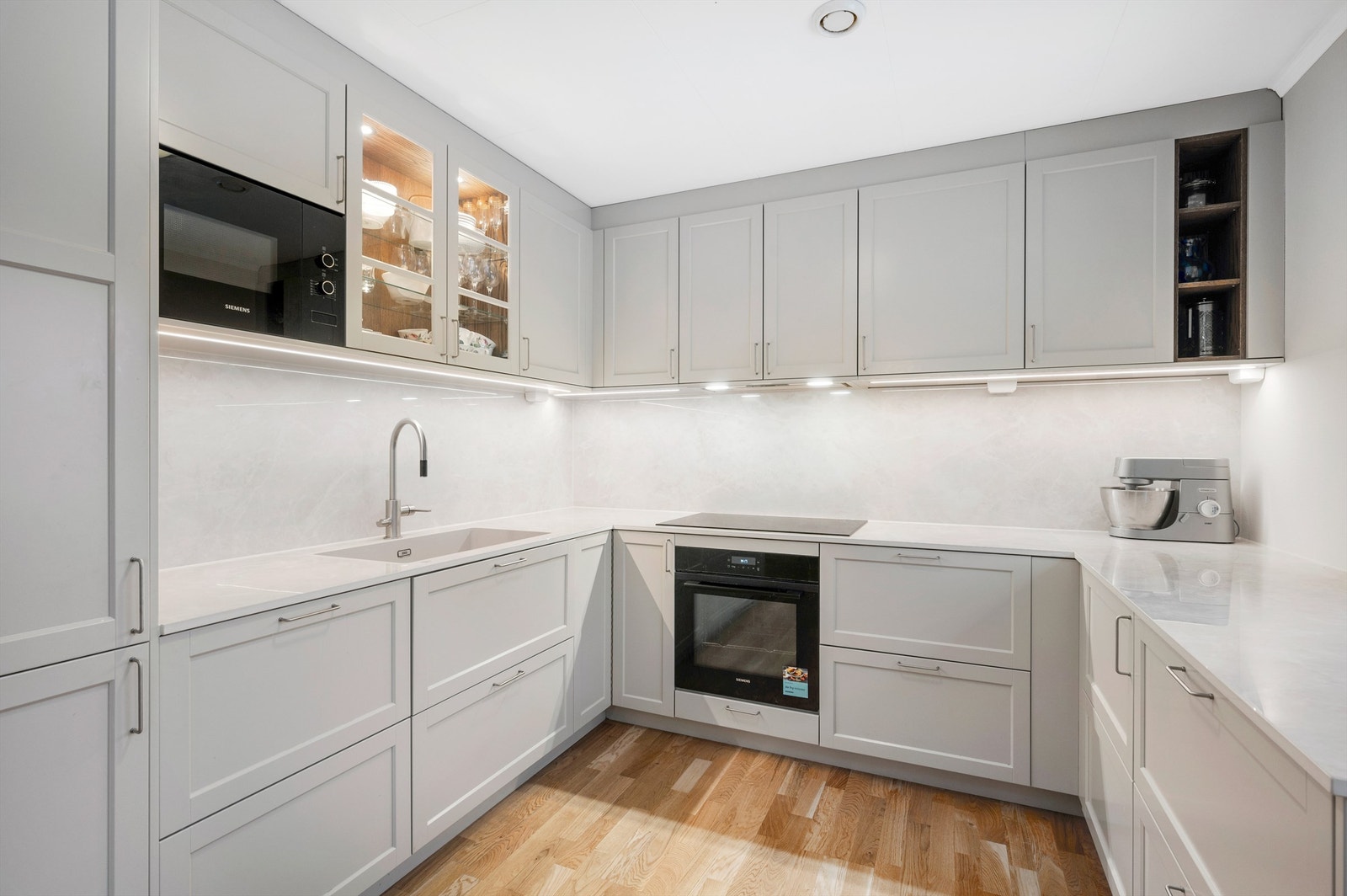 Nydelig kjøkkeninnredning fra Drømmekjøkkenet med integrert stekeovn, platetopp, oppvaskmaskin, mikrobølgeovn og kjøleskap med fryser. Legg merke til praktisk benkeskapsbelysning. Galleribilde