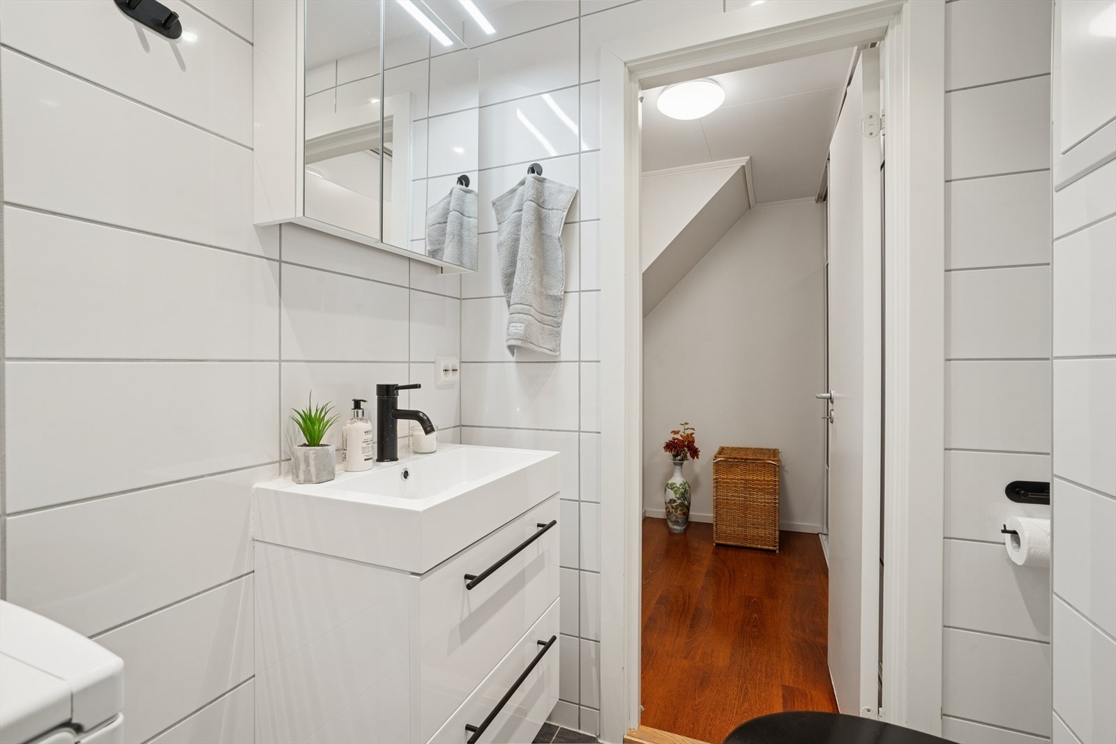 Innredningen består av en servant med underskuffer, speilskap, et vegghengt toalett og et dusjhjørne med svingbare dusjvegger i sort glass. Galleribilde