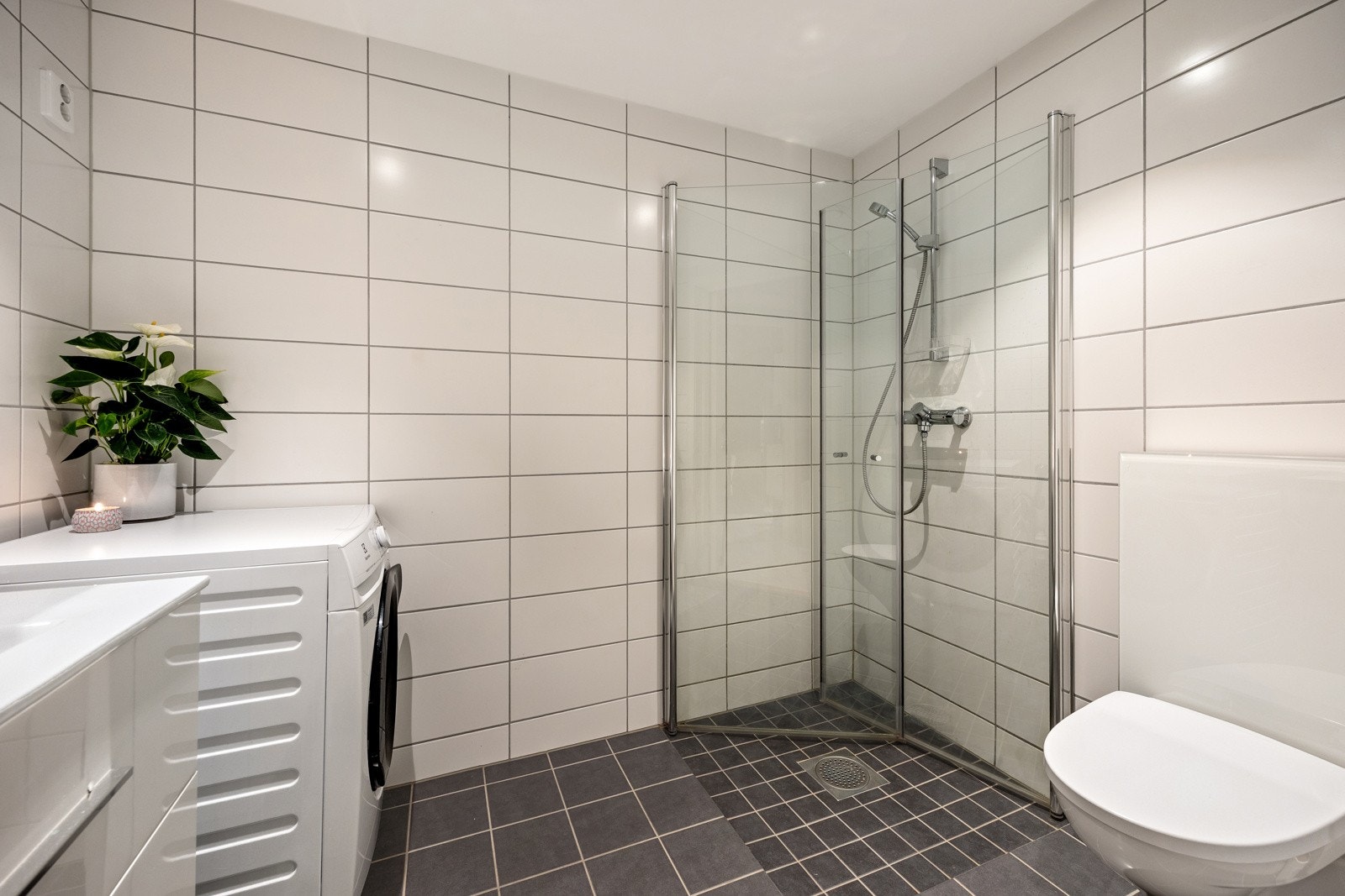 Videre har badet et separat dusjhjørne med innfellbare glassdører og hånddusj. Det er avsatt plass, samt opplegg for vaskemaskin og tørketrommel i vaskesøyle. Himlingen er pent lyssatt med downlights. Galleribilde