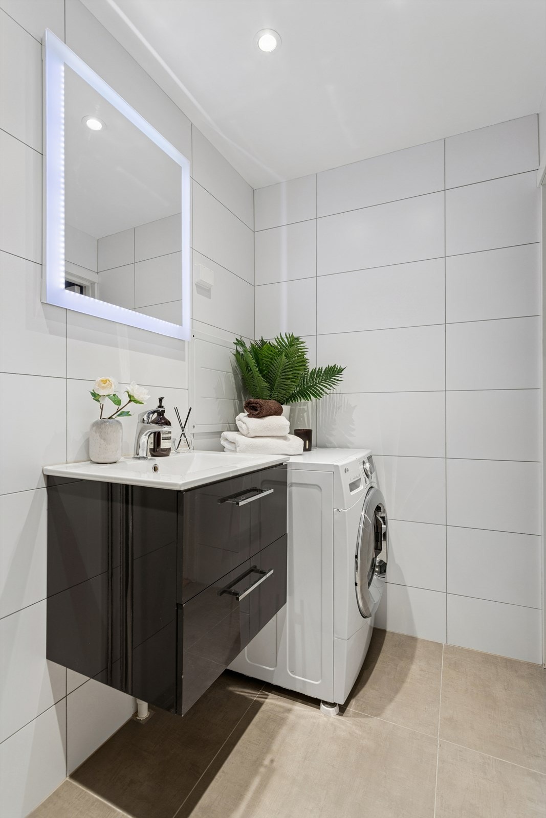 Badet er utstyrt med servant og servantskap med glatte skuffefronter i grå høyglans. Speil med integrert kantbelysning over servant gir et moderne uttrykk og godt lys. Galleribilde