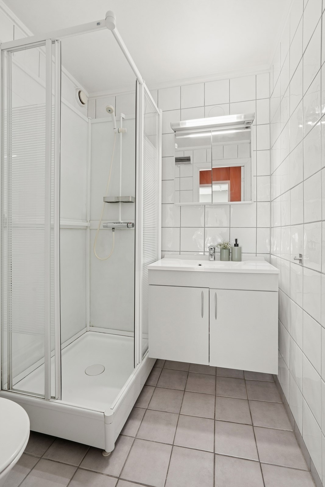 Effektivt utnyttet baderom med vegghengt speilskap, lysarmatur og nøytrale overflater. Galleribilde