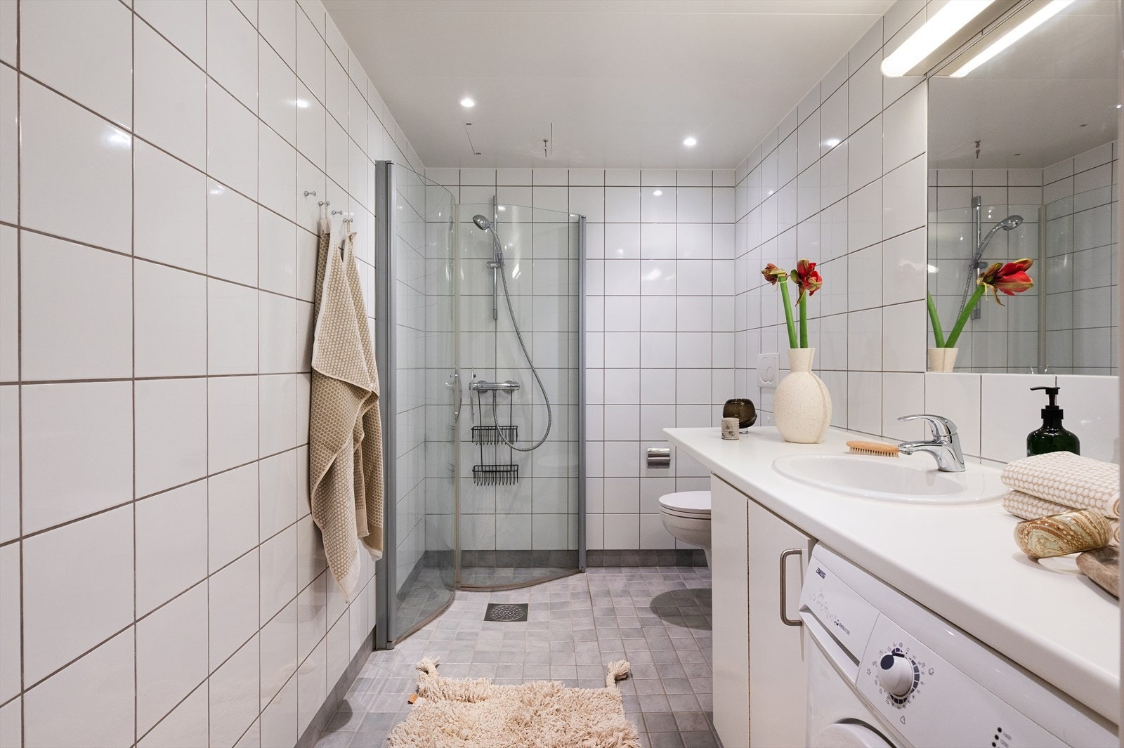 Pent og tidsriktig baderom med vegghengt toalett, servant nedfelt i benkeplate med tilhørende innredning samt dusjhjørne med svingbare glassdører. Galleribilde