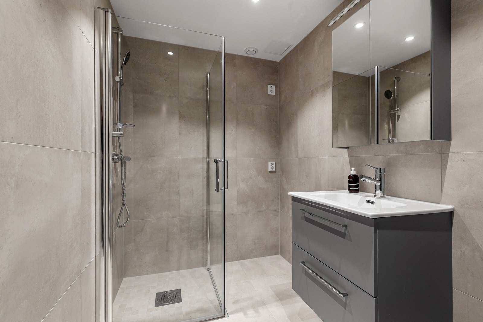 Badet er innredet med dusjhjørne med glassdører, vegghengt toalett og innredning med nedsunket servant med speilskap Galleribilde