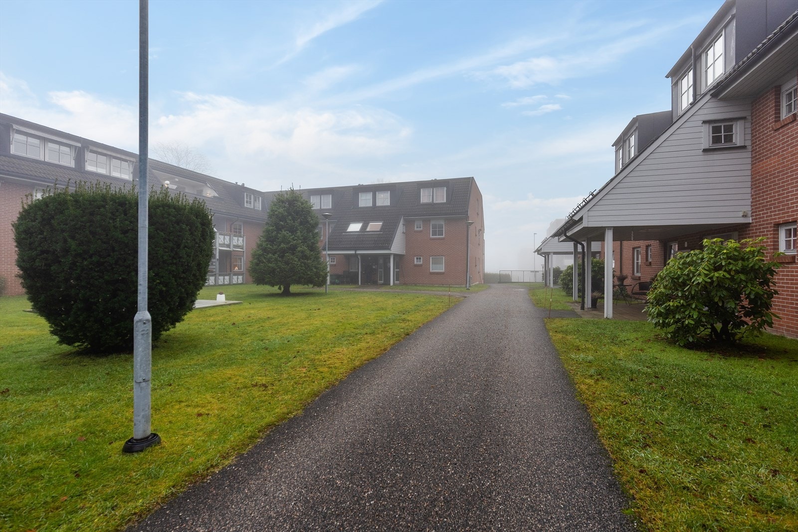 Sameiets tomt er pent opparbeidet med beplantet felles boligtun med plen og asfalterte gangstier. Galleribilde