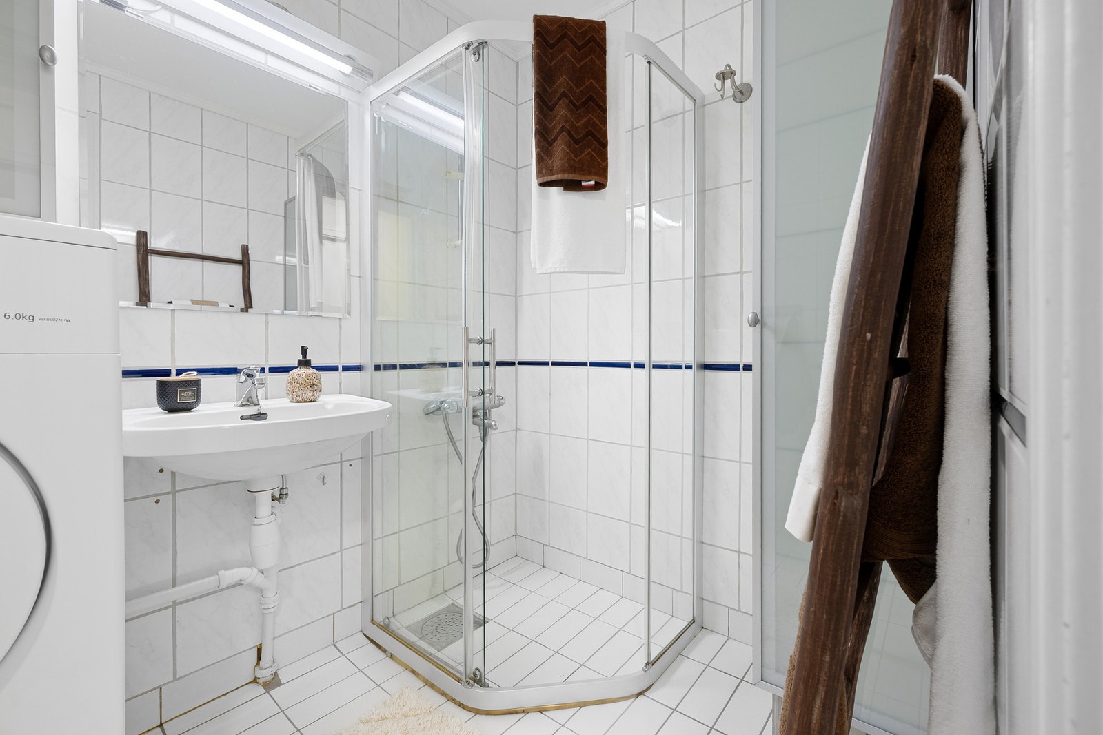 Flislagt baderom utstyrt med dusjhjørne i glass og servant med speil og overlys. Galleribilde