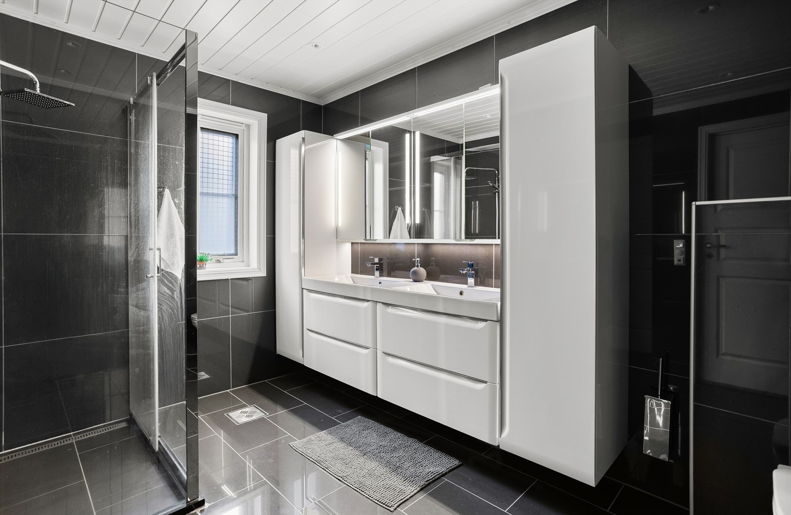 Badet i første etasje har mørke fliser, dusjhjørne og dobbelt servantskap. Galleribilde