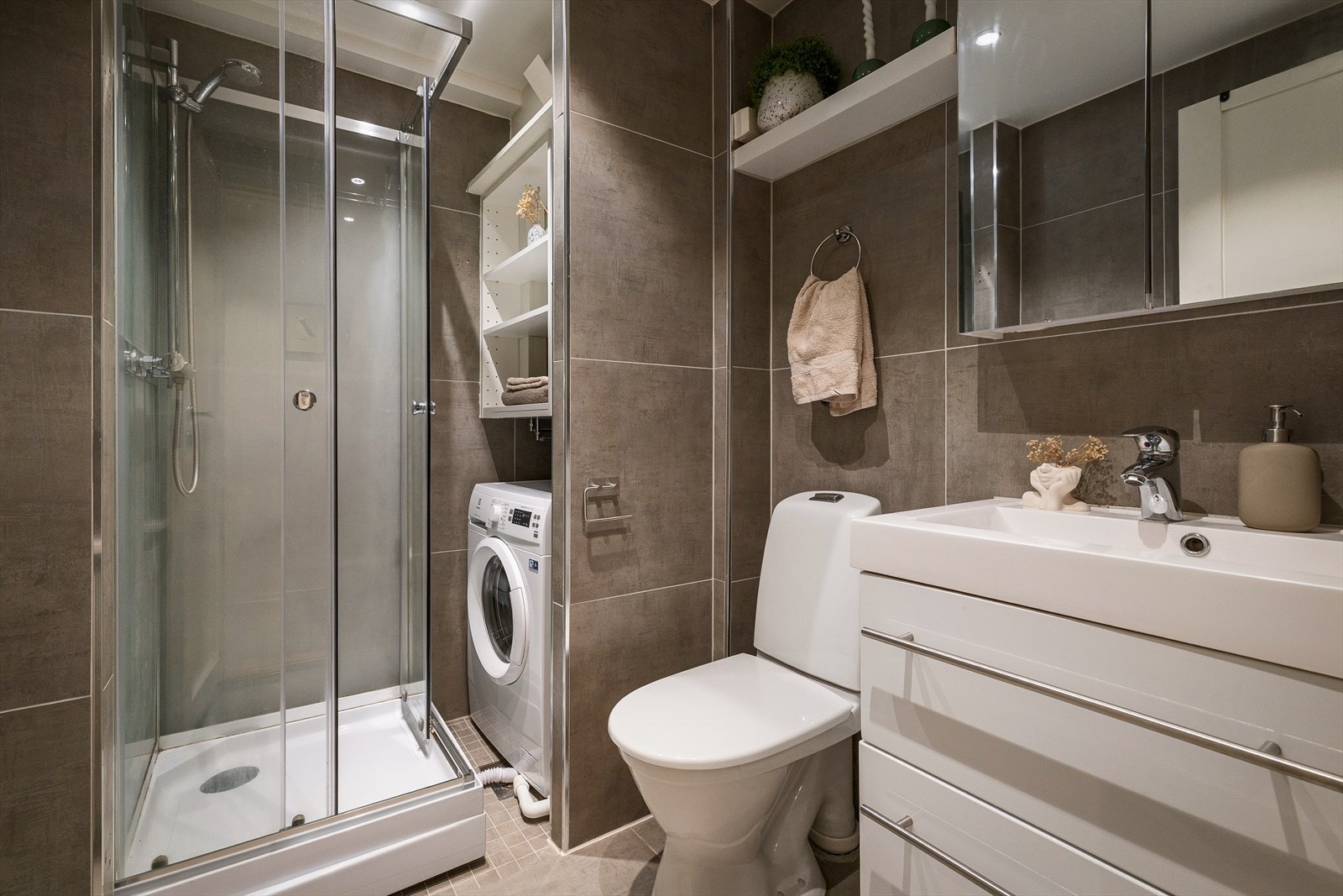 Pent flislagt baderom med varmekabler i gulv. Badet har gulvstående toalett og dusjkabinett. Det er opplegg for vaskemaskin Galleribilde