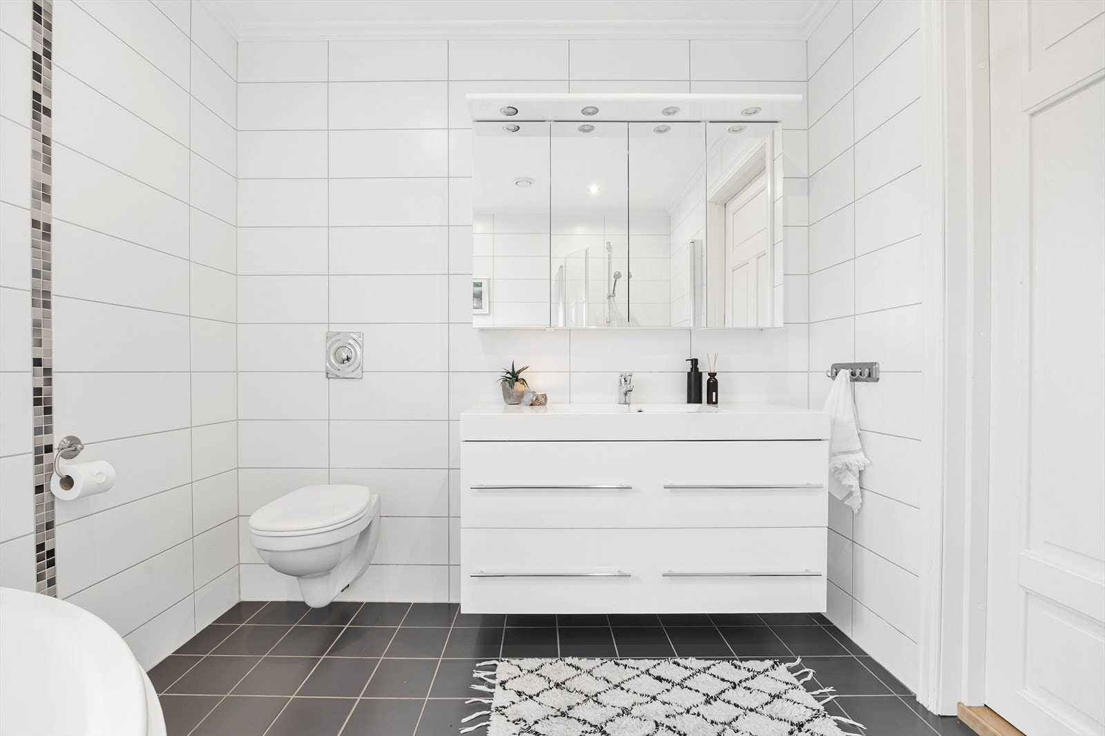 Badet er utstyrt med vegghengt toalett, servant med skuffer, dusjnisje med innfellbare glassdører og badekar. Galleribilde