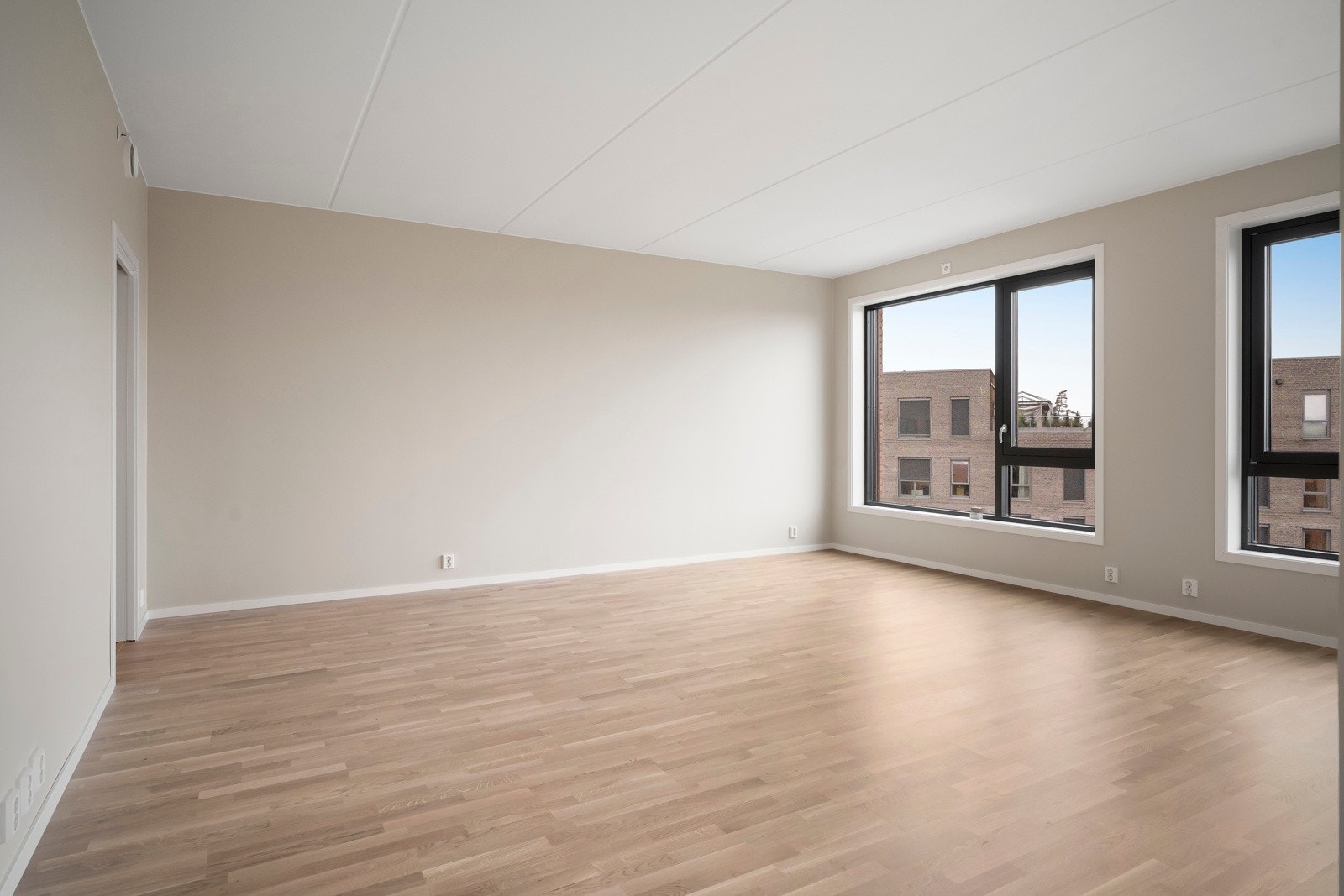 Romslig stue med god takhøyde og store gulv-til-tak-vindusflater i flere himmelretninger som slipper inn rikelig med naturlig lys. Lys hvitpigmentert eikeparkett og vannbåren varme i gulvet gir en behagelig og innbydende atmosfære. Galleribilde