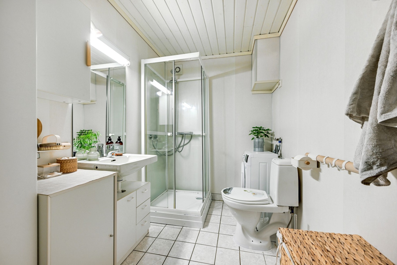 Flislagt bad med dusjkabinett, toalett, servant og opplegg til vaskemaskin Galleribilde