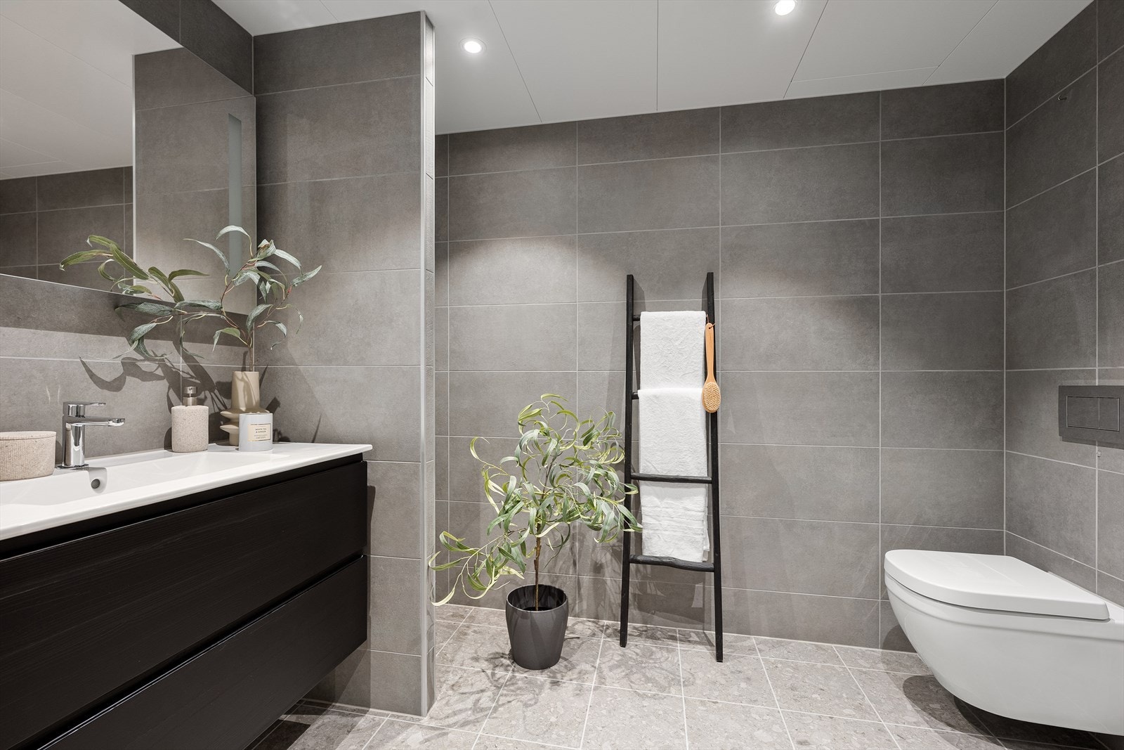 Badet er delikat innredet med grå fliser på gulv og vegg. Her er det varmekabler på gulvet. Galleribilde