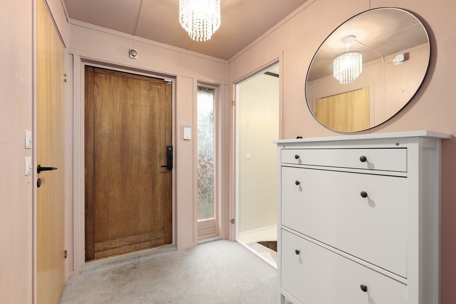 Entreen har teppe på gulv og malte plater på vegger. Her er det inngang til toalettrom og trapp ned til boligens underetasje. Galleribilde