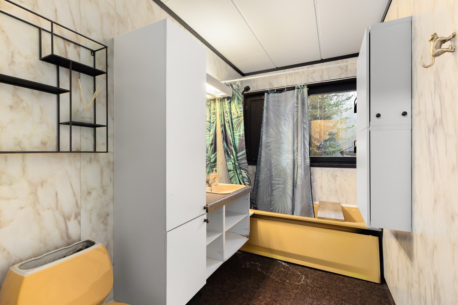 Bad fra byggeår med vinylbelegg på gulv og baderomsplater på vegger. Her er det toalett, badekar med dusjhåndtak på vegg og innredning med benkeplate med nedfelt vask og skap. Galleribilde